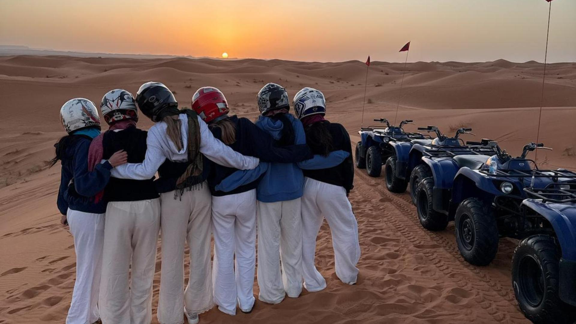 Group of friends watching the sunset over the Sahara Desert, with ATVs parked nearby.