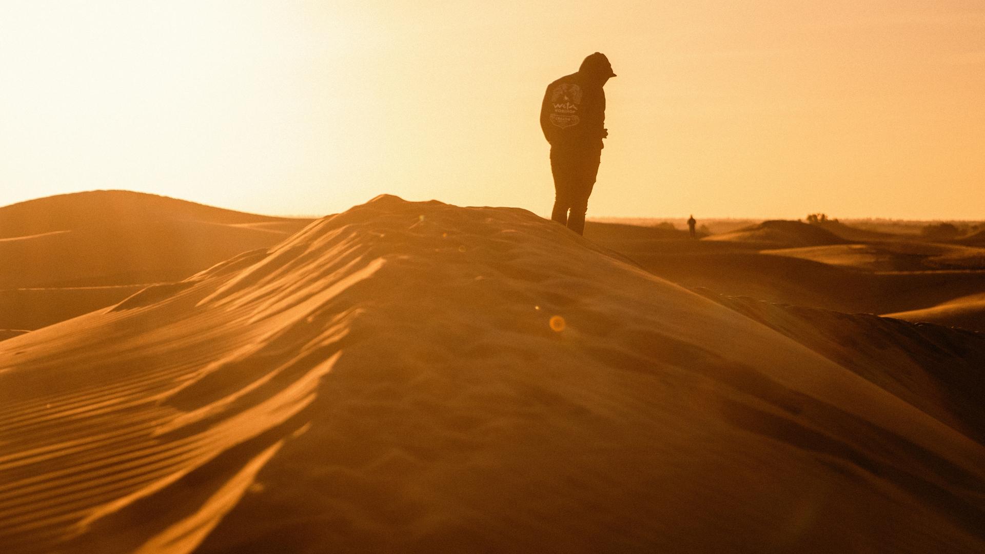 A silhouette of a person standing on a sand dune at sunset in the Sahara Desert, Morocco.